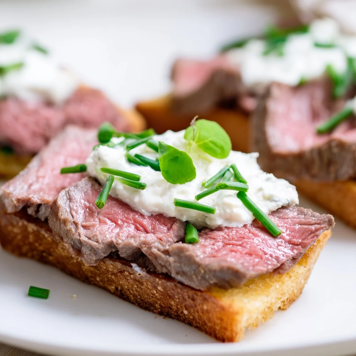 Golden, crispy toast points topped with seared beef slices and creamy horseradish sauce, garnished with fresh chives.