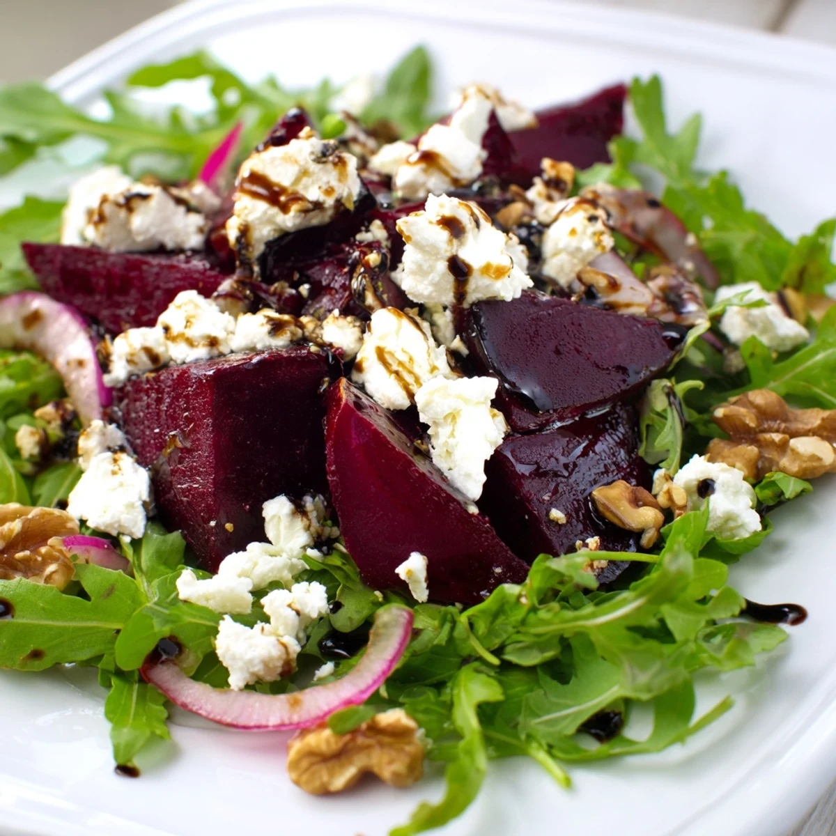 Vibrant roasted beet and walnut salad with peppery arugula and goat cheese crumbles, drizzled with balsamic vinaigrette on a white plate.