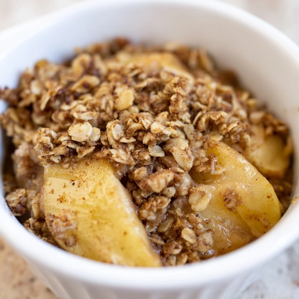 A close-up of baked apple crisp with granola topping revealing tender cinnamon apples and a golden, crunchy oat crust on a rustic table.