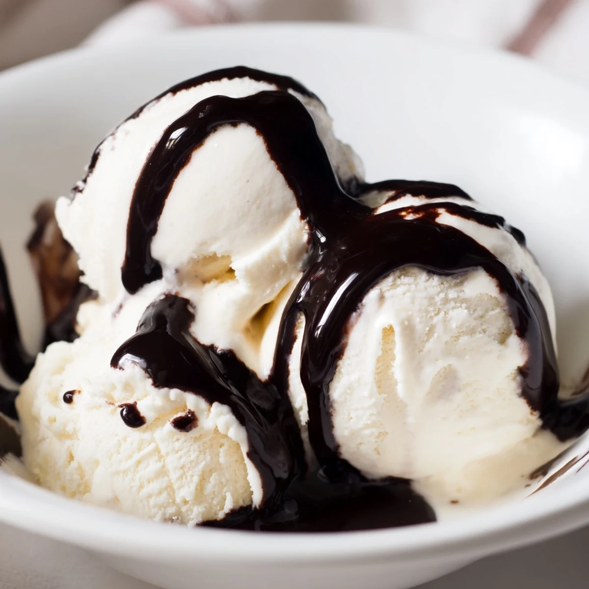 Decadent chocolate syrup drizzles over creamy vanilla ice cream in dessert bowls.