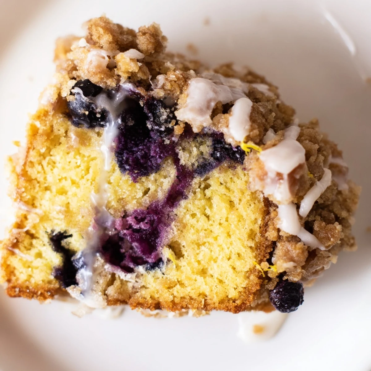 A close-up of a warm slice of Lemon Blueberry Coffee Cake shows juicy blueberries and a moist crumb.