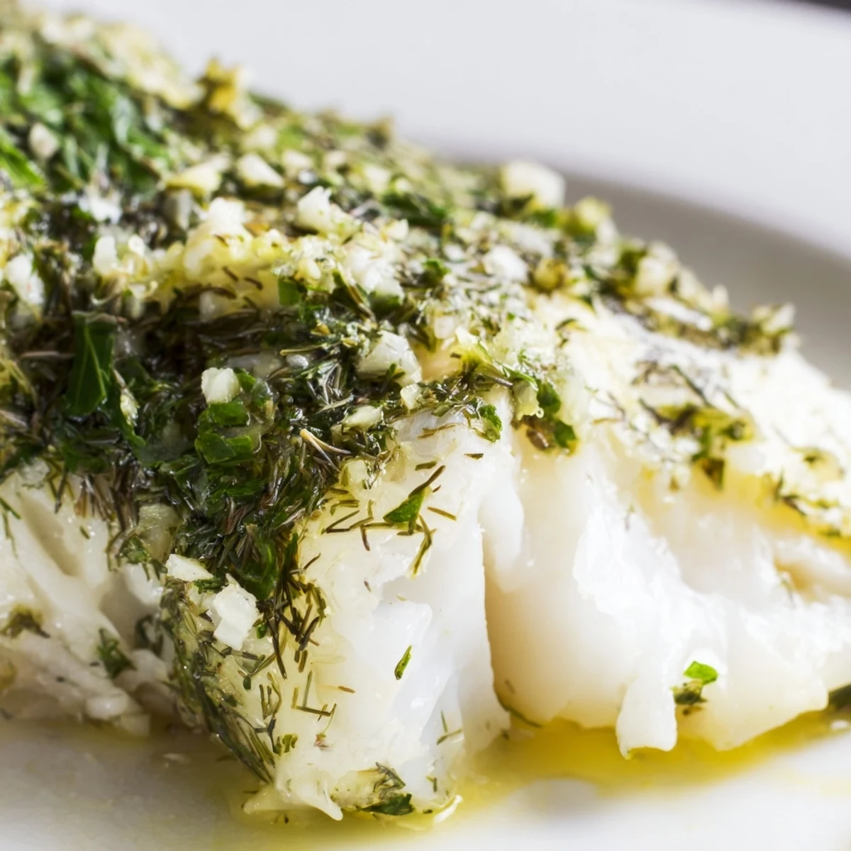Freshly baked halibut fillets with herbs and butter, glistening on a plate with lemon wedges.