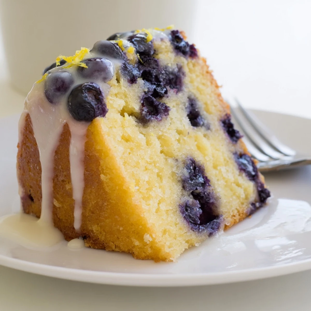 Bright lemon blueberry cake glazed and topped with extra berries, a perfect spring dessert on a rustic wooden table.