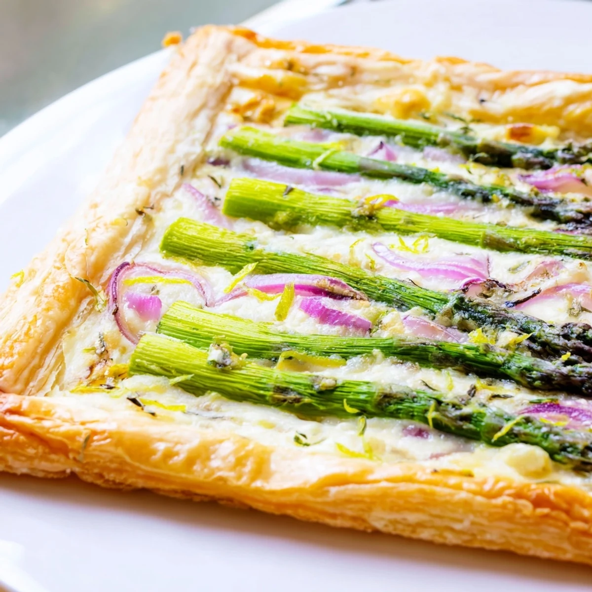 Slice of warm Green Asparagus Puff Pastry Tart served on a white plate, showcasing the creamy cheese layer and tender asparagus tips.