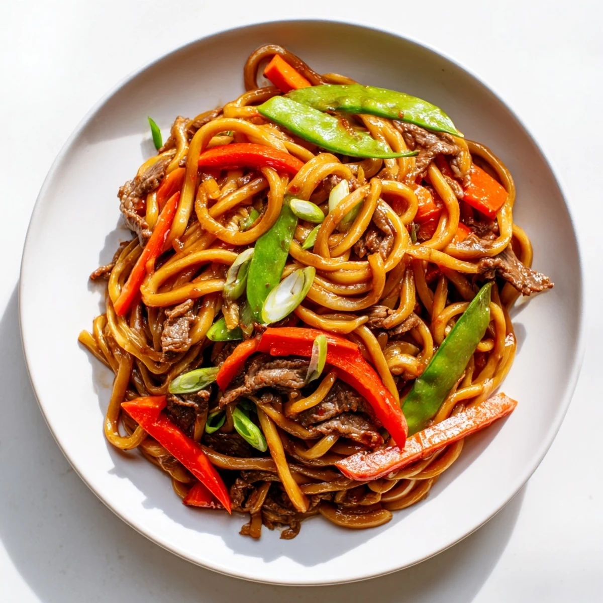 Steaming bowls of spicy beef stir fry with udon noodles feature tender meat and colorful vegetables.