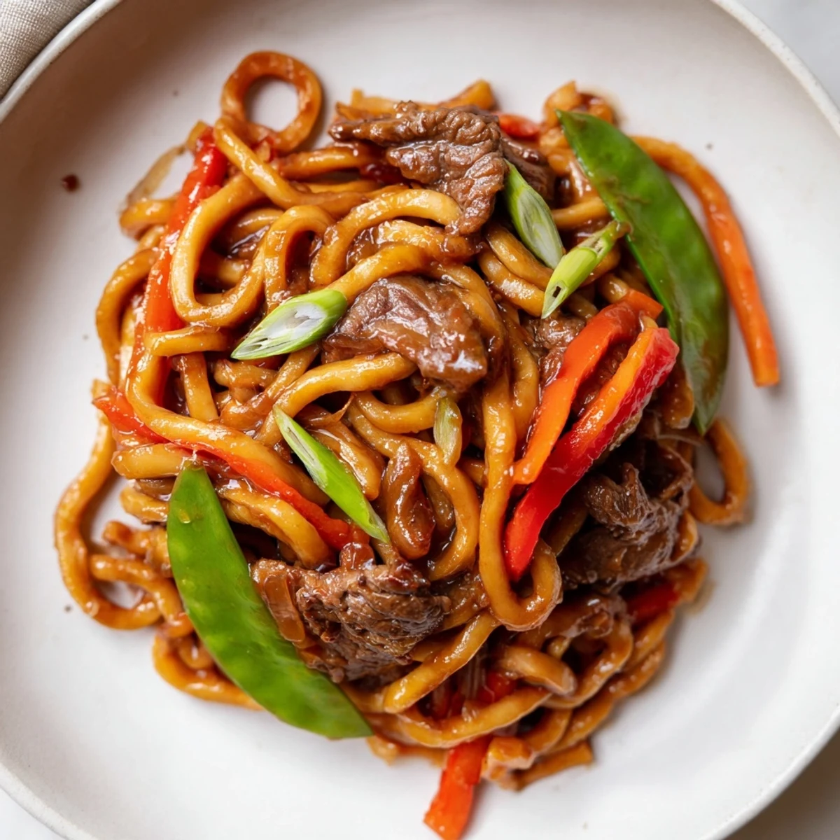 Sizzling spicy beef stir fry with udon noodles served steaming hot, garnished with fresh scallions.