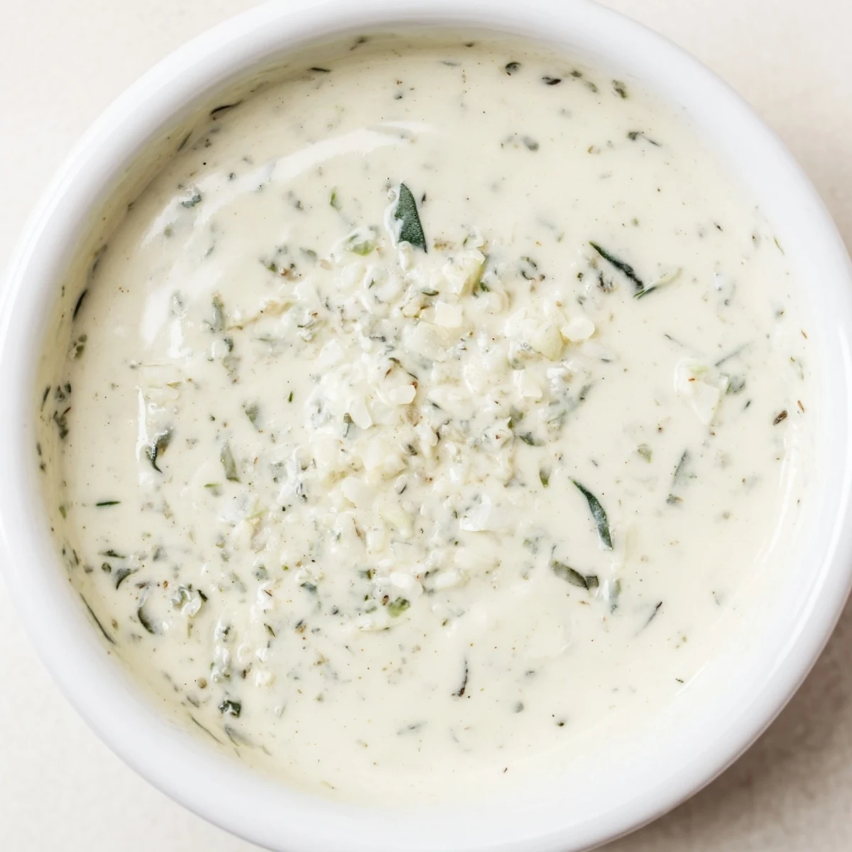 Creamy herb salad dressing drizzled over crisp greens, with fresh parsley, dill, and chives visible in the vibrant green mixture.  