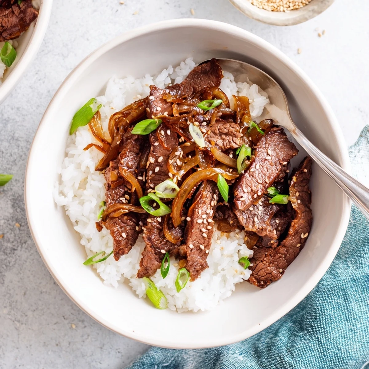 Golden-brown beef strips glazed in savory sauce rest on fluffy white steamed rice, garnished with fresh green onions and toasted sesame seeds in a rustic ceramic bowl.