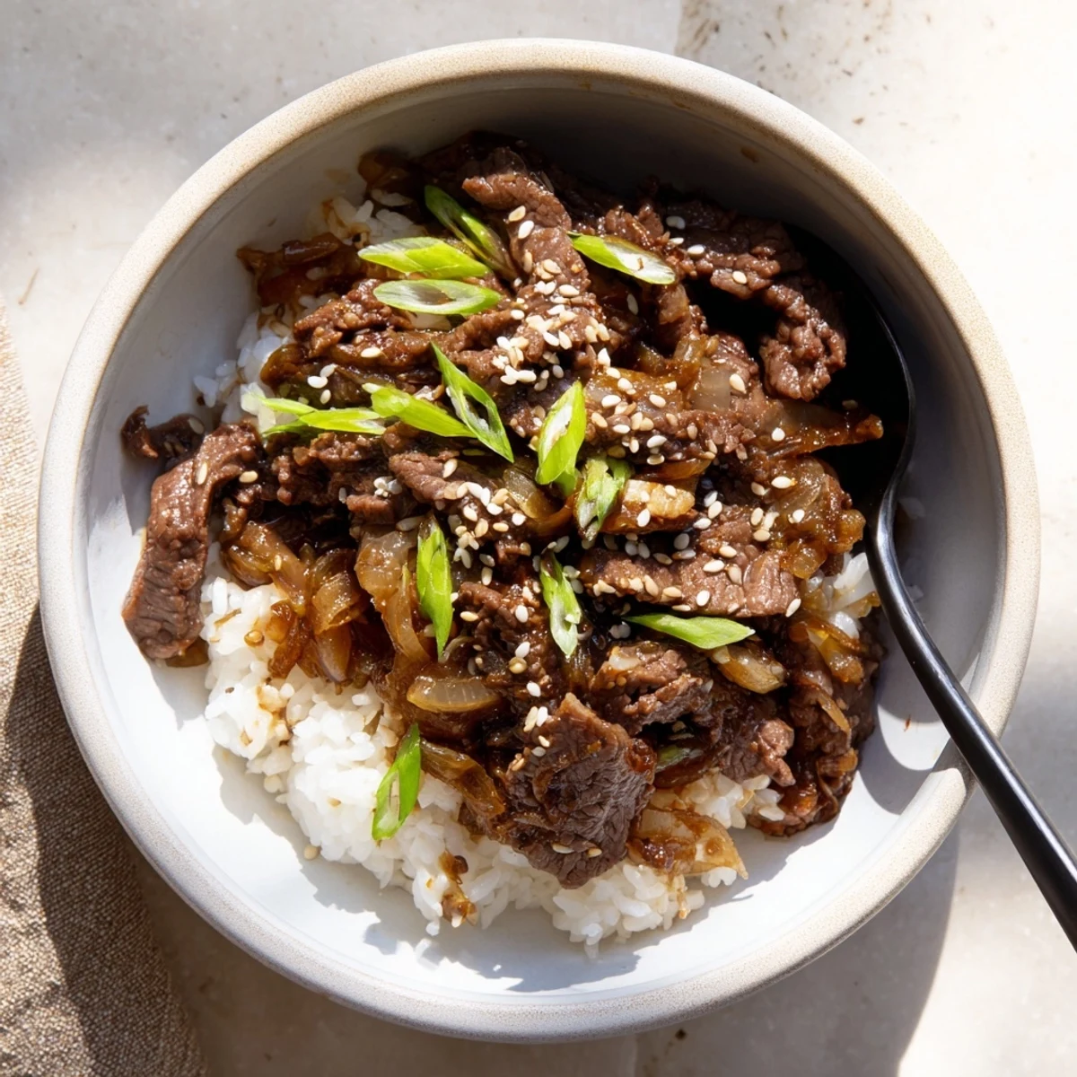 Ready-to-serve Asian-inspired Beef Bowl with Steamed Rice features juicy meat, caramelized onions, and pickled ginger garnish, ideal for a quick weeknight dinner in the United States.