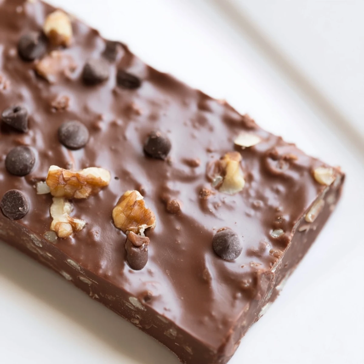 A close-up of a freshly baked Chocolate Treat Bar Sweet bar, highlighting melted chocolate chips and toasted walnuts on a rich, gooey layer.