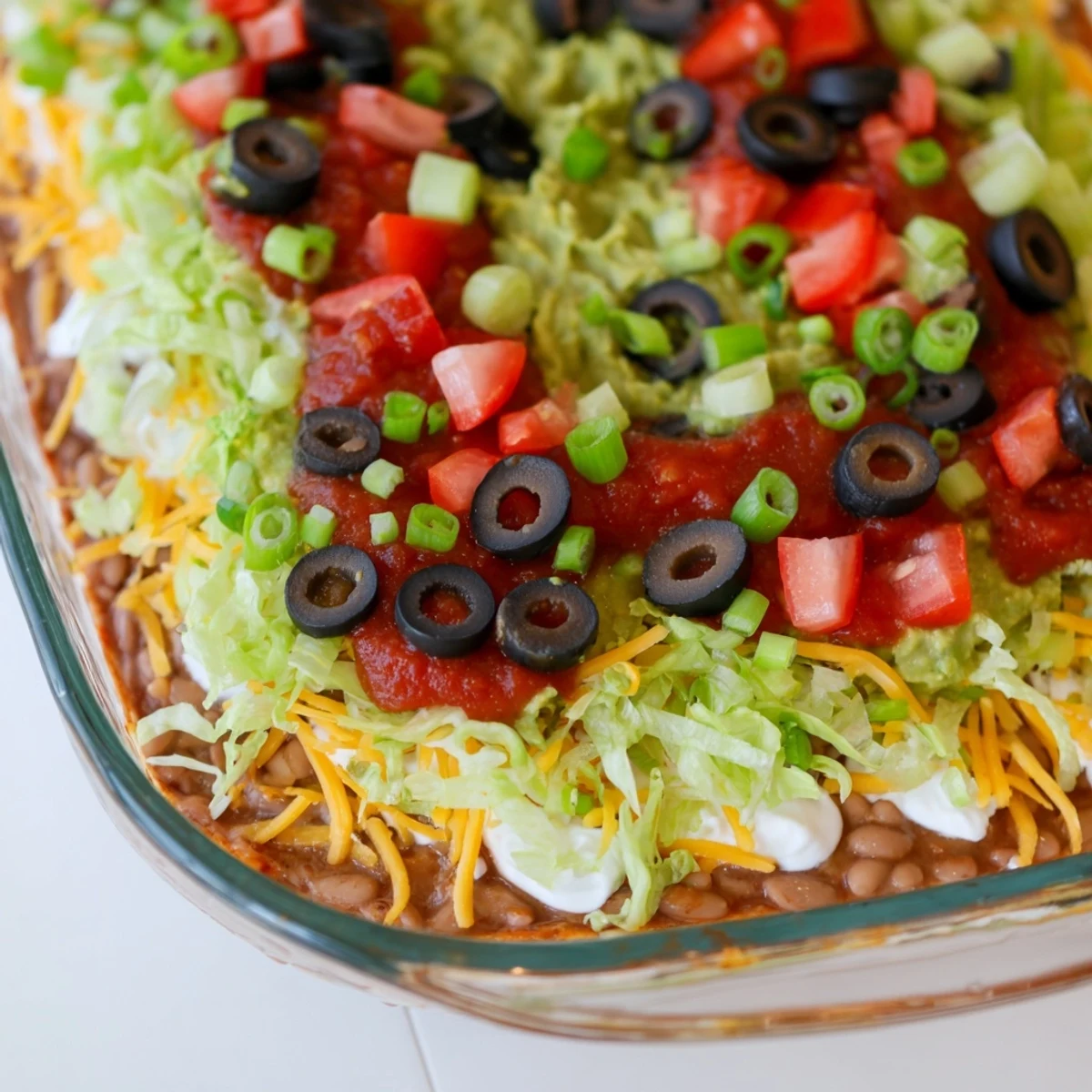 A top-down view of the Ultimate Seven Layer Taco Dip, featuring vibrant layers of guacamole, sour cream, and shredded cheese, served with crispy tortilla chips.