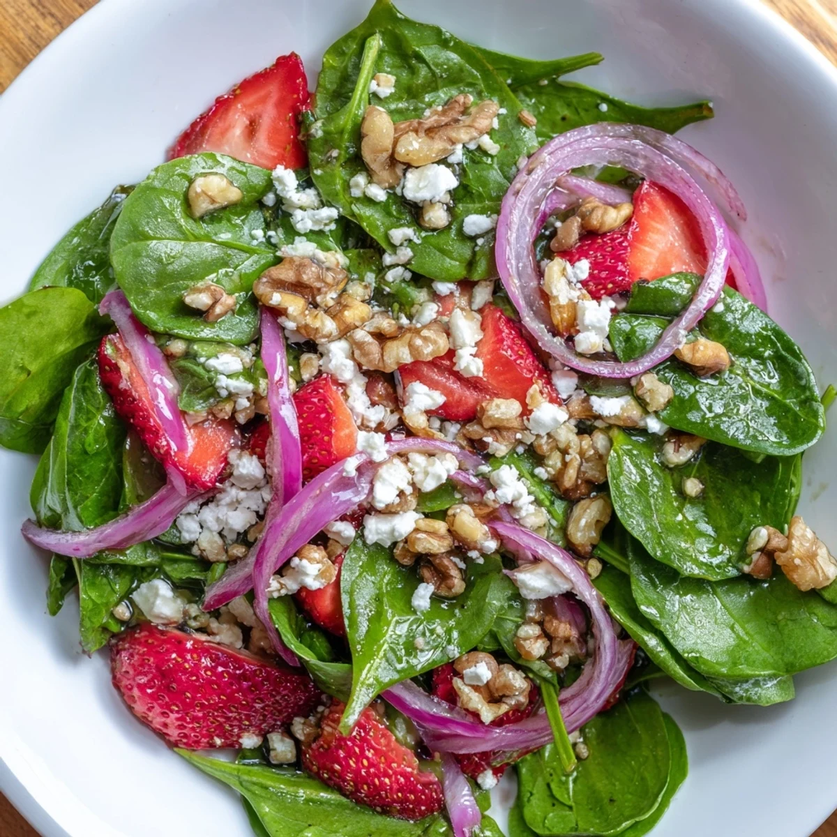 Close-up of freshly tossed Strawberry Walnut Spinach Salad with Balsamic, showcasing glistening greens, juicy berries, and crunchy toasted nuts on a rustic table.