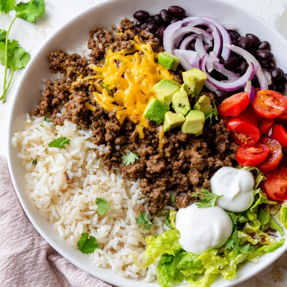 Vibrant Beef Burrito Bowls with Rice and Beans topped with creamy avocado, cheese, and fresh cilantro.