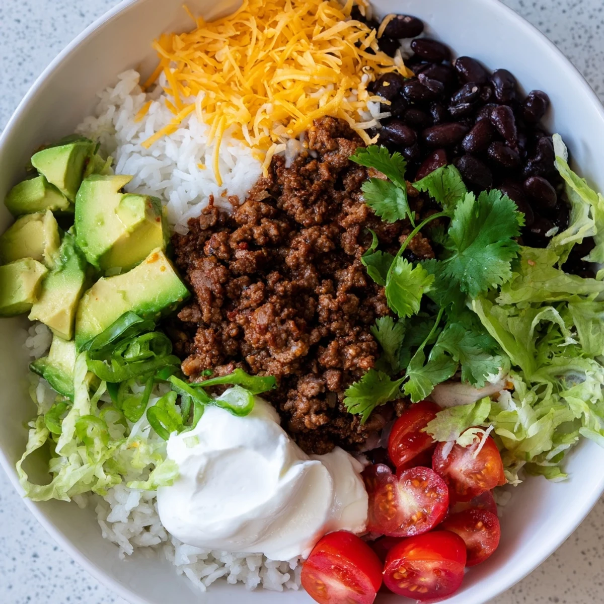 An overhead view of Beef Burrito Bowls with Rice and Black Beans garnished with cilantro, cheese, and lime wedges on a rustic table.