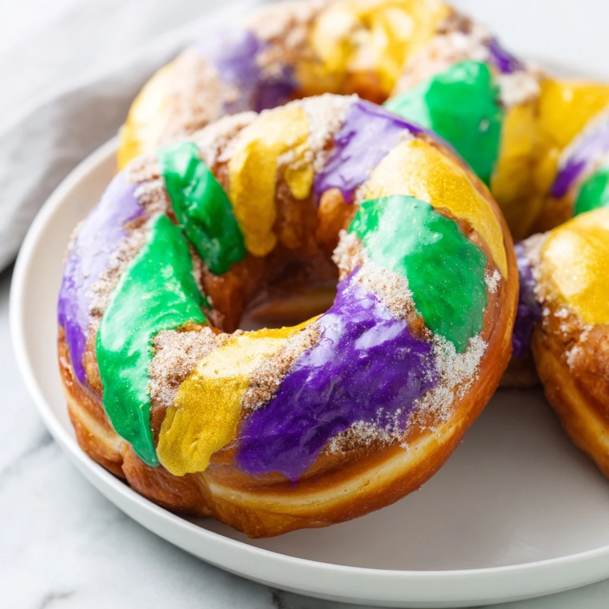 Freshly fried Mardi Gras King Cake Donuts arranged on a wire cooling rack with festive holiday decorations in the background.  