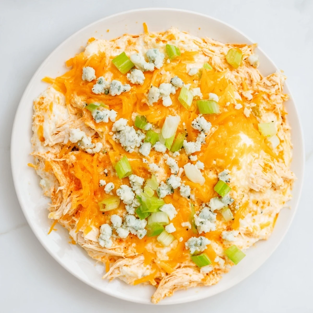 Bubbling golden Keto Buffalo Chicken Dip fresh from the oven, with celery sticks for dipping beside a serving spoon.