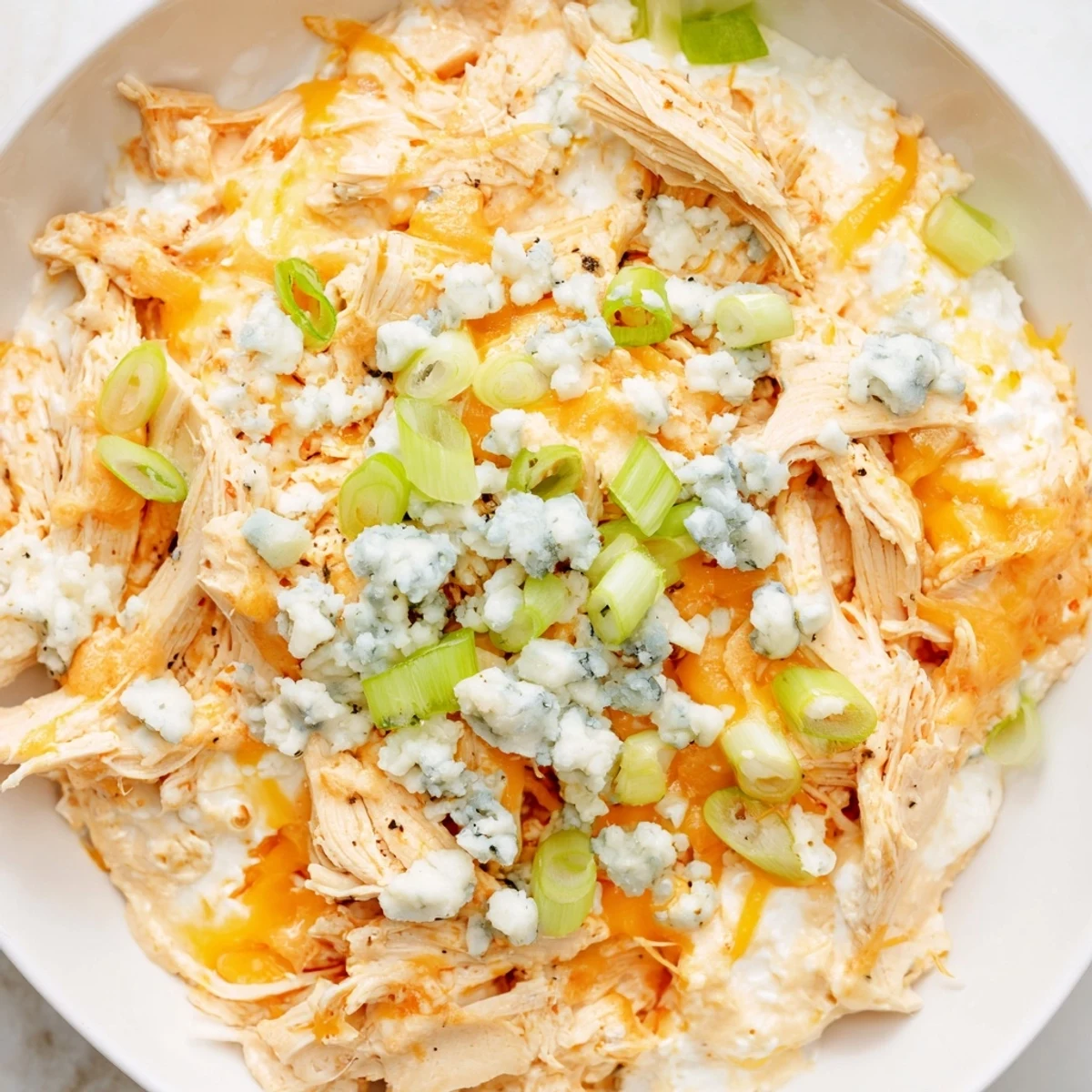 An overhead view of creamy Keto Buffalo Chicken Dip, topped with melted cheese and chopped green onions on a rustic table.