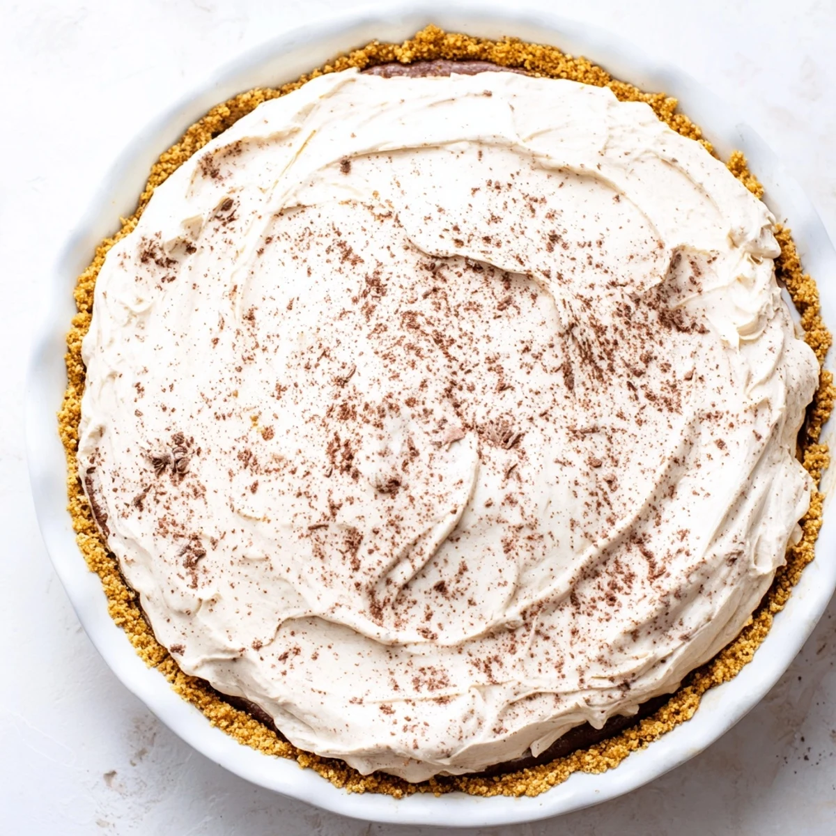 Creamy keto cold brew coffee pie in a golden almond flour crust, topped with fluffy whipped cream and a dusting of cocoa powder.