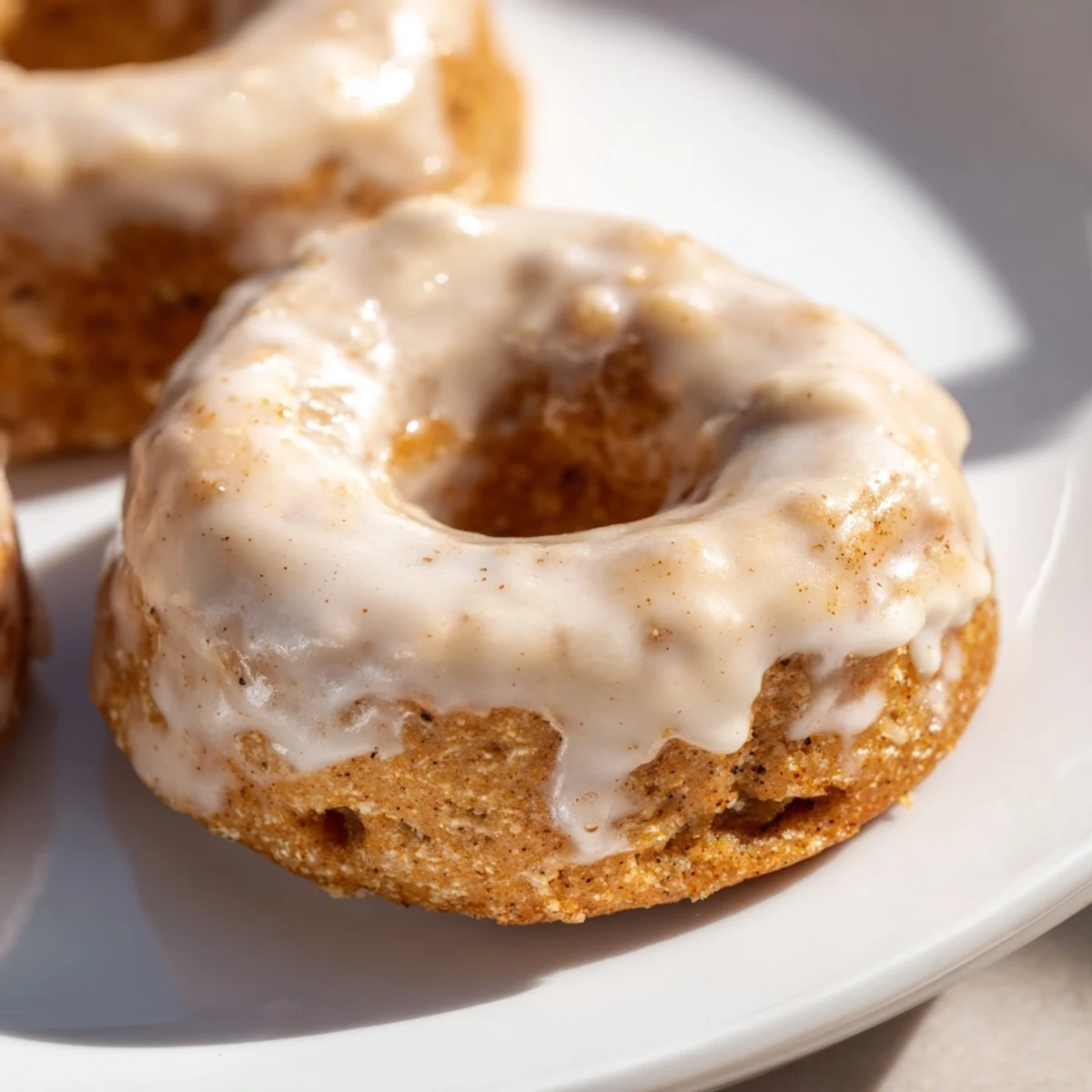 Golden Baked Banana Bread Donuts glistening with a sweet glaze and topped with banana slices on a rustic wood table.