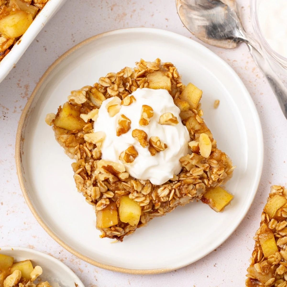 Squares of Baked Apple Oatmeal With Greek Yogurt are served with walnuts and a drizzle of maple syrup.  