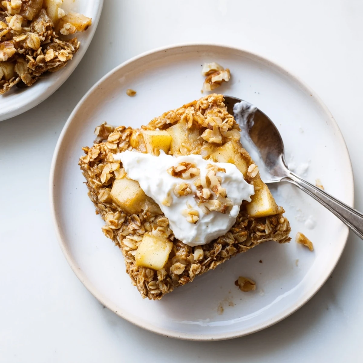Freshly baked apple oatmeal with Greek yogurt topping sits in a white ceramic dish, warm and inviting.  