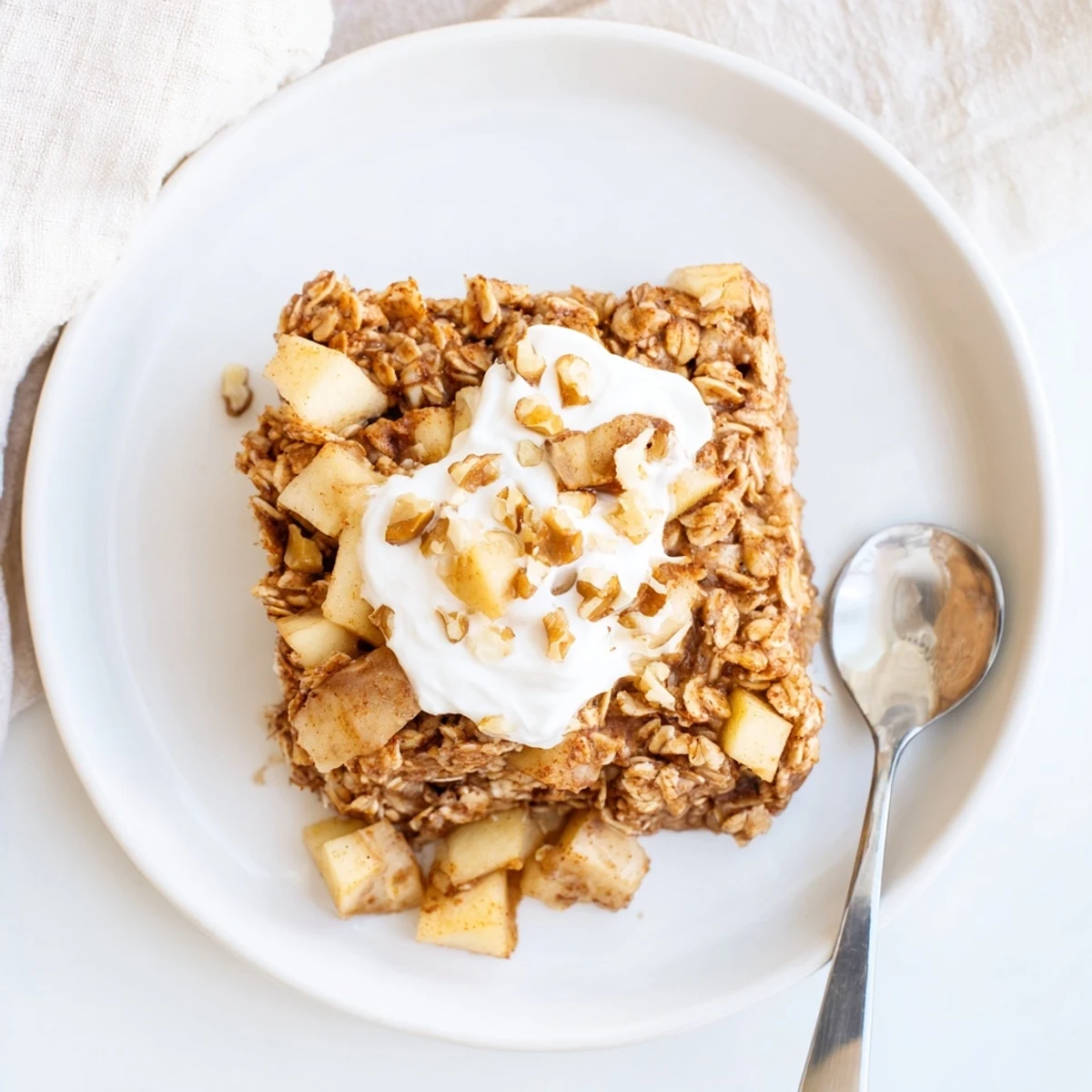 A close-up of Baked Apple Oatmeal With Greek Yogurt highlights tender baked oats and spiced apple chunks.