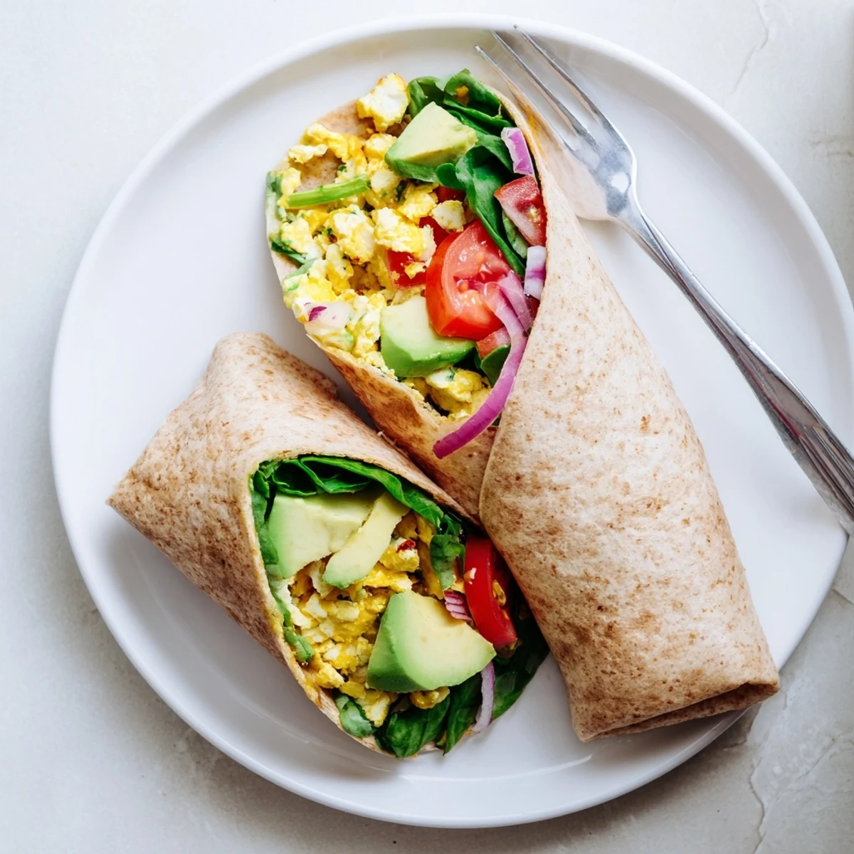 Folding a High Protein Breakfast Wrap with Cottage Cheese and Avocado filled with fluffy eggs, diced tomatoes, and fresh spinach.