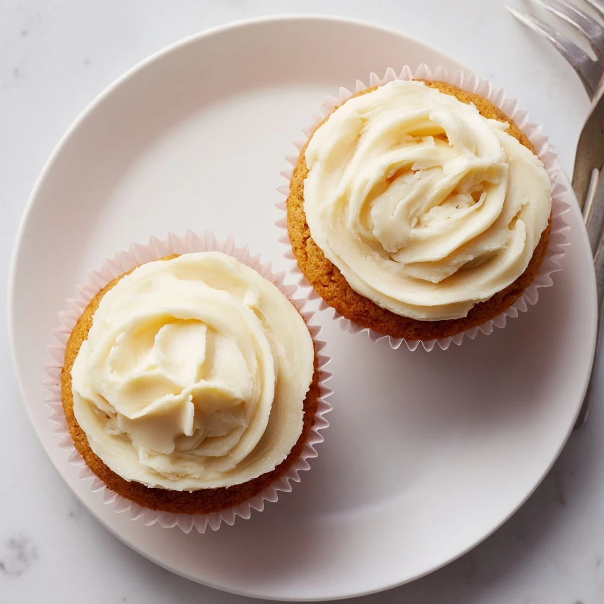A close-up of fresh-baked Elderflower Cupcakes, the creamy white buttercream frosting swirled high, a single edible violet garnish on top, bathed in soft natural light.