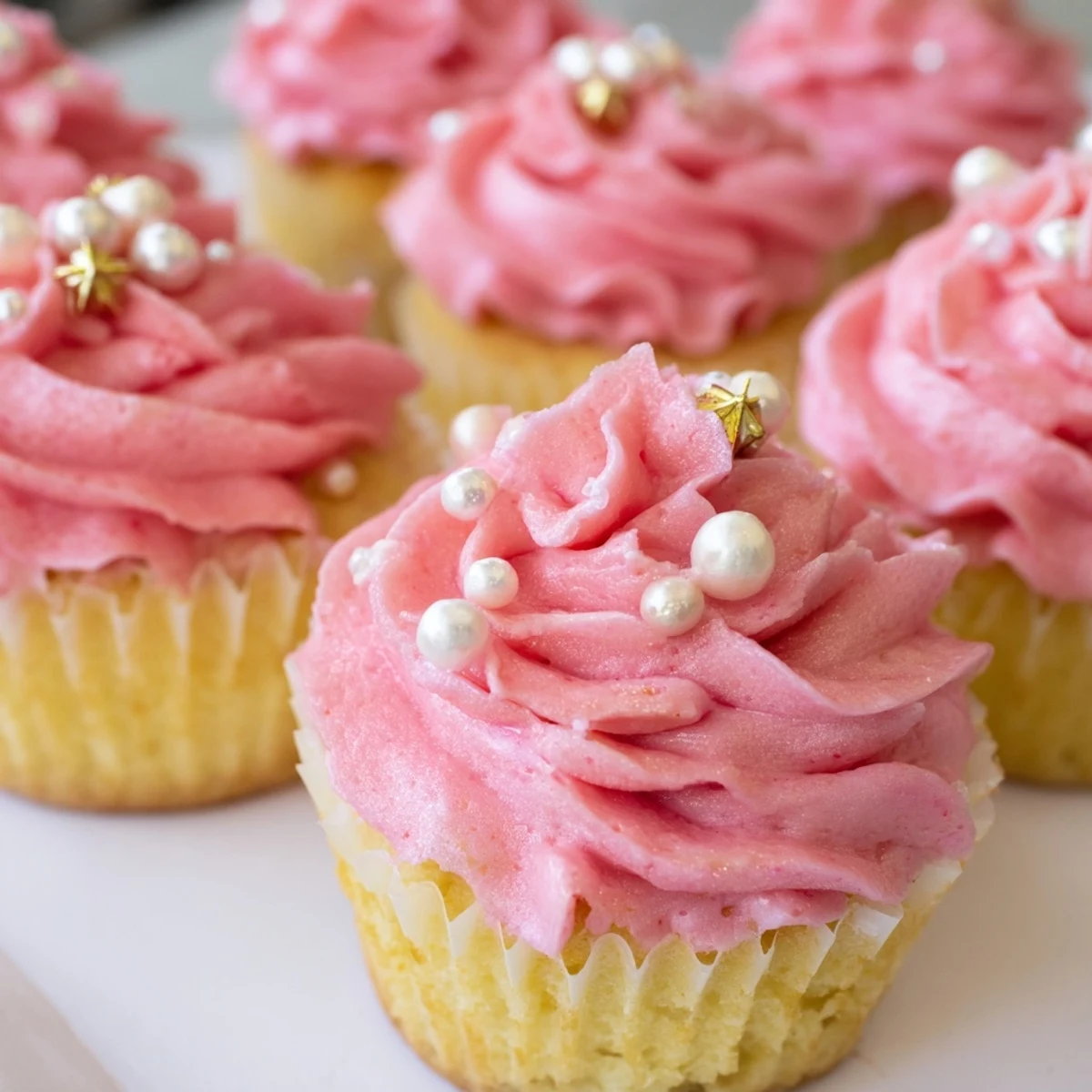 Overhead view of Girl Baby Shower Cupcakes arranged in a circle, with pale pink buttercream peaks and a light dusting of shimmering edible glitter.