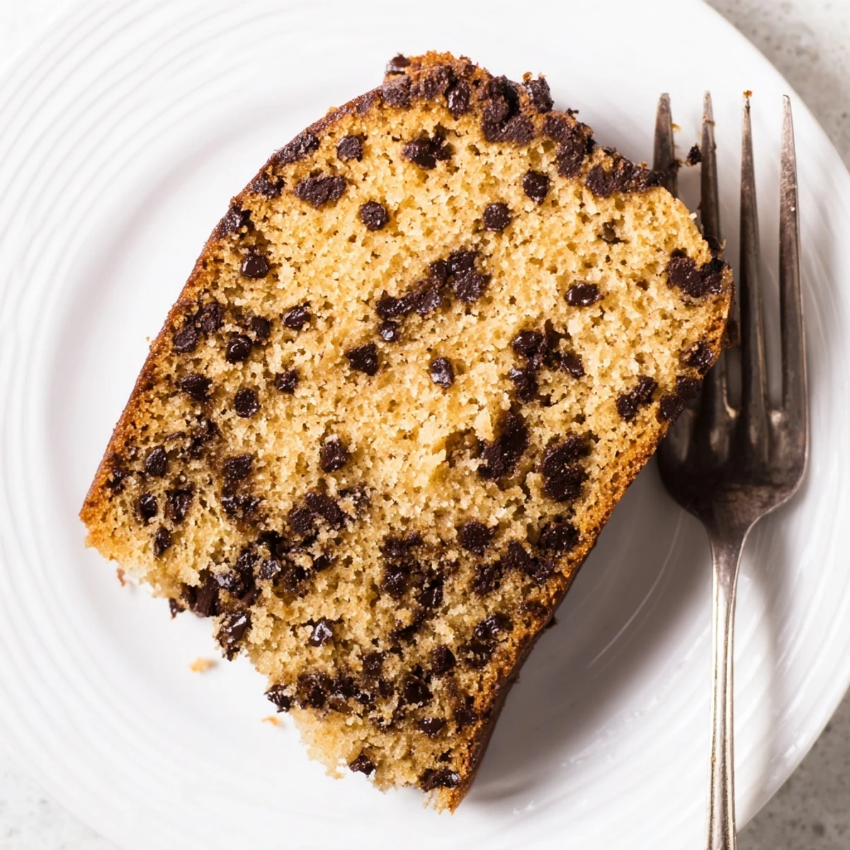 A slice of warm Chocolate Chip Cake on a plate, showcasing melted chips and a tender crumb ready for dessert.