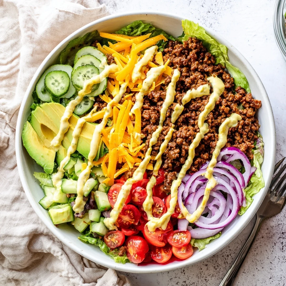 Close-up of Burger Bowls with seasoned ground beef, crisp romaine, cheddar, and bright toppings on a white plate.