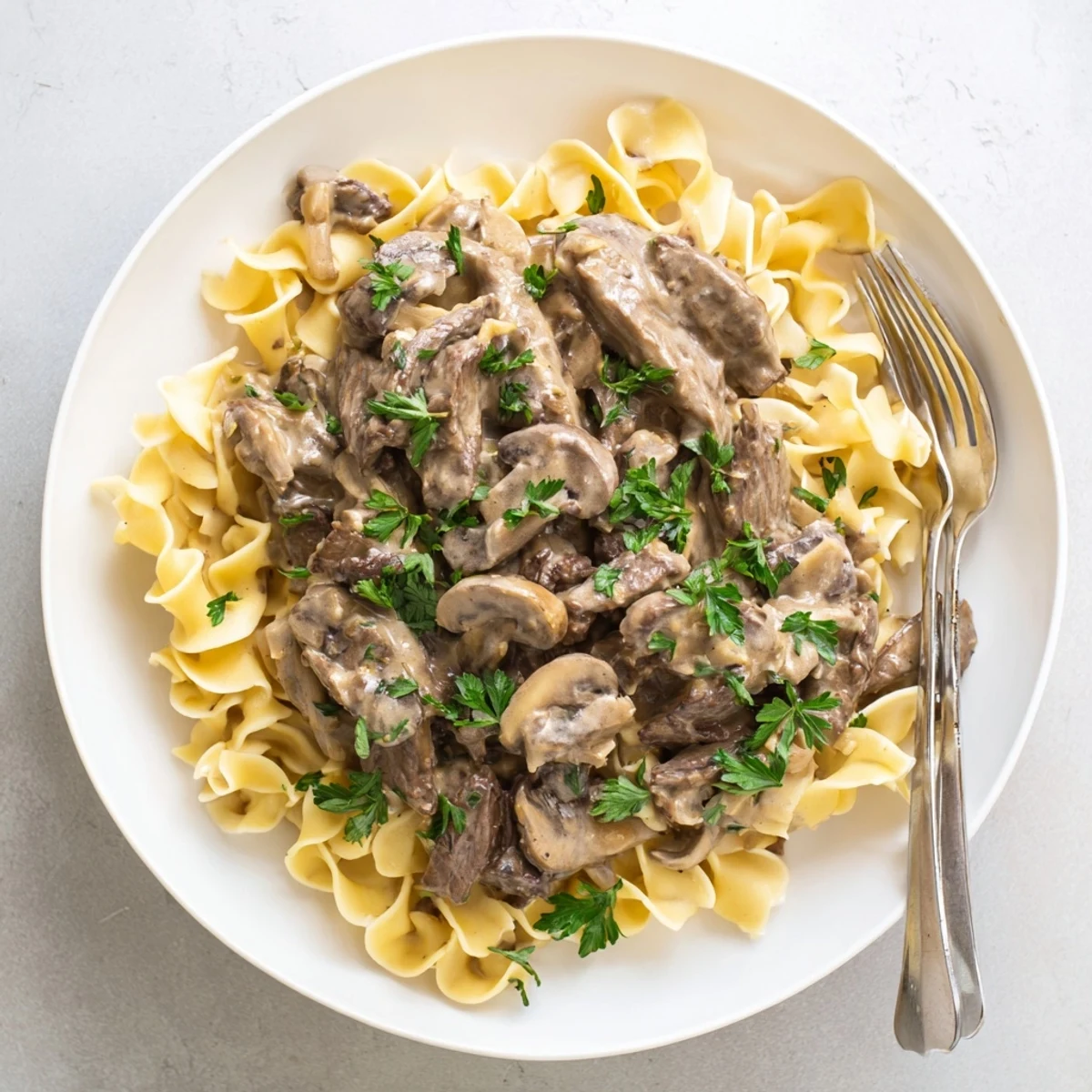 Tender beef strips in rich sour cream sauce with earthy sliced mushrooms over noodles