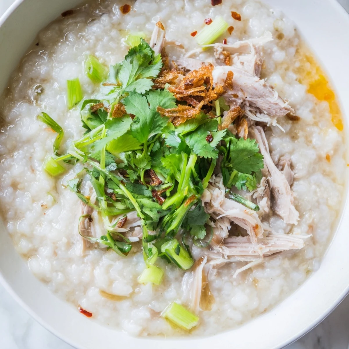Steaming bowl of savory rice porridge with shredded turkey meat, ginger, and drizzled chili oil