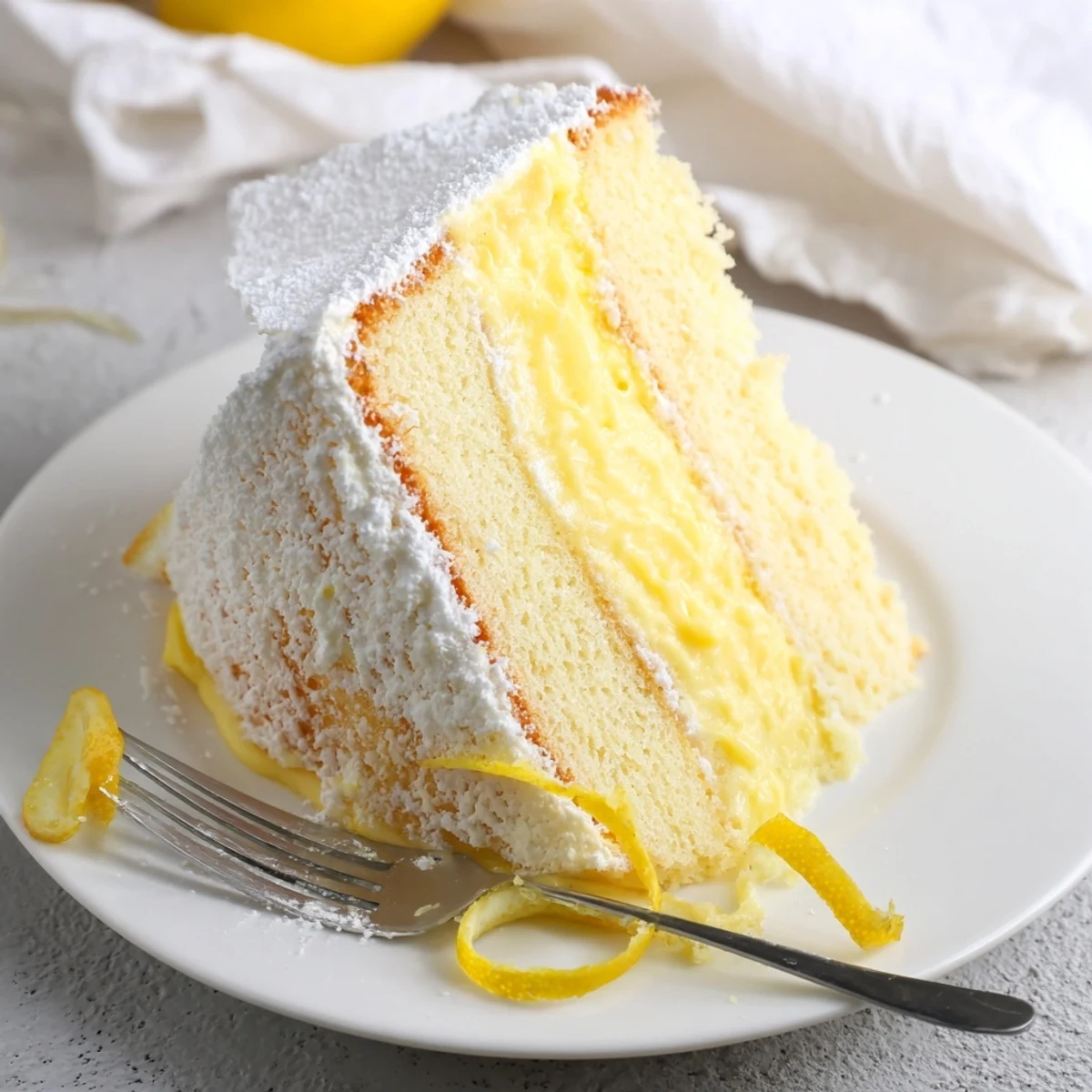 Fluffy Italian Grandmas Lemon Custard Cake dusted with powdered sugar and fresh lemon curl garnish