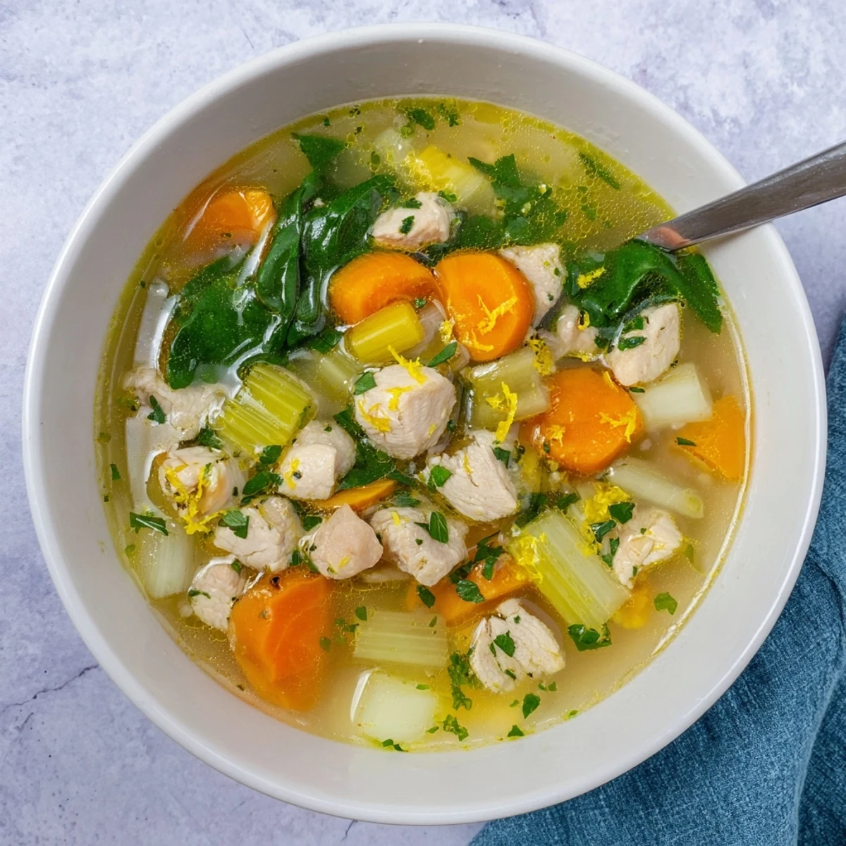 Close-up of wholesome Mediterranean chicken soup brightened with fresh lemon zest, herbs, and tender chicken pieces in a white bowl