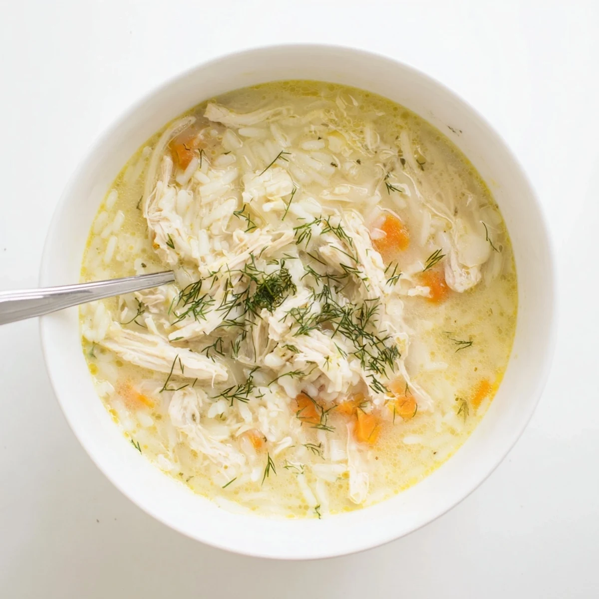 Steamy bowl of avgolemono Greek lemon chicken soup featuring silky textured broth with shredded chicken pieces and rice topped with vibrant green herbs