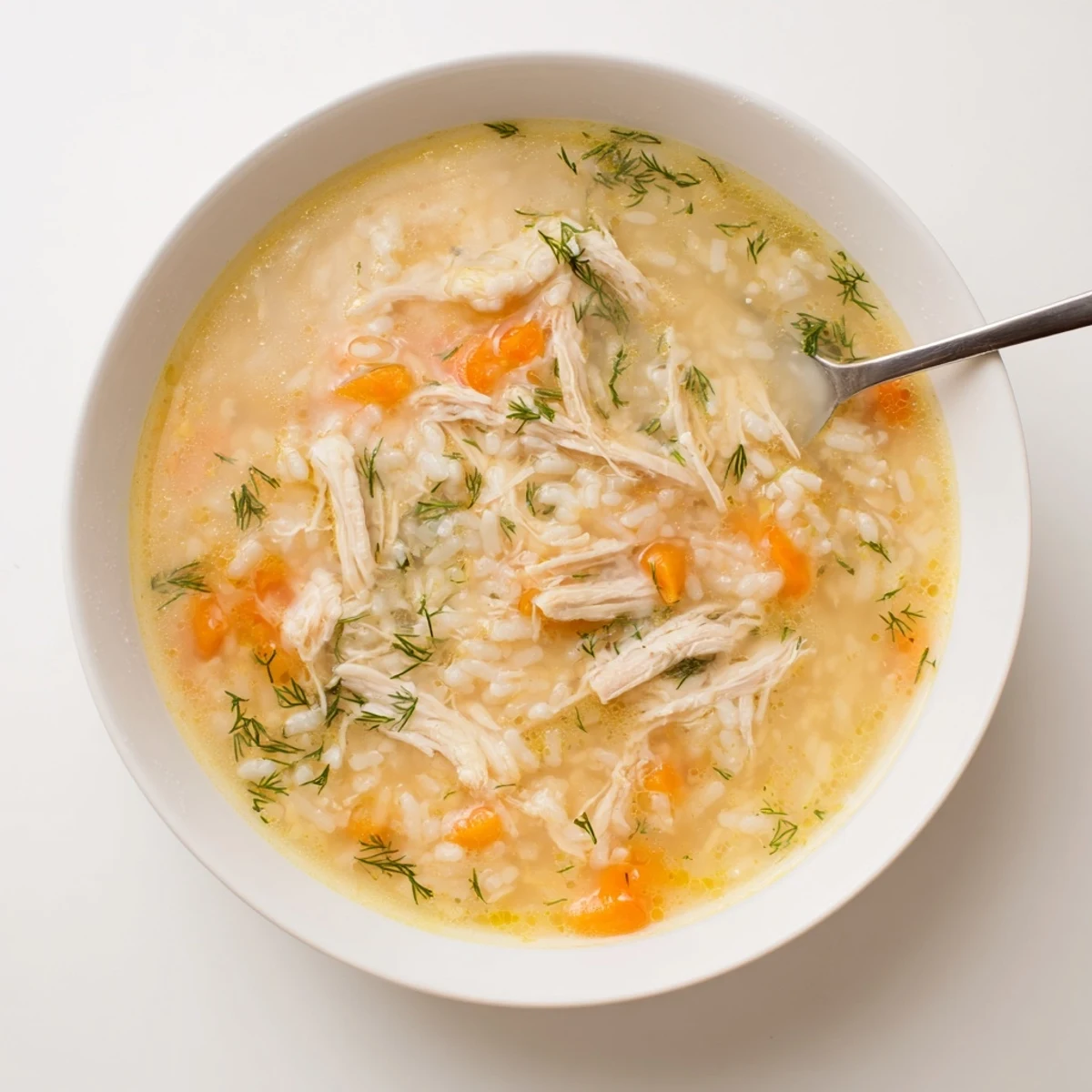 Homemade avgolemono Greek lemon chicken soup ladled into a white serving bowl showing rich creamy consistency with tender chicken and rice suspended throughout