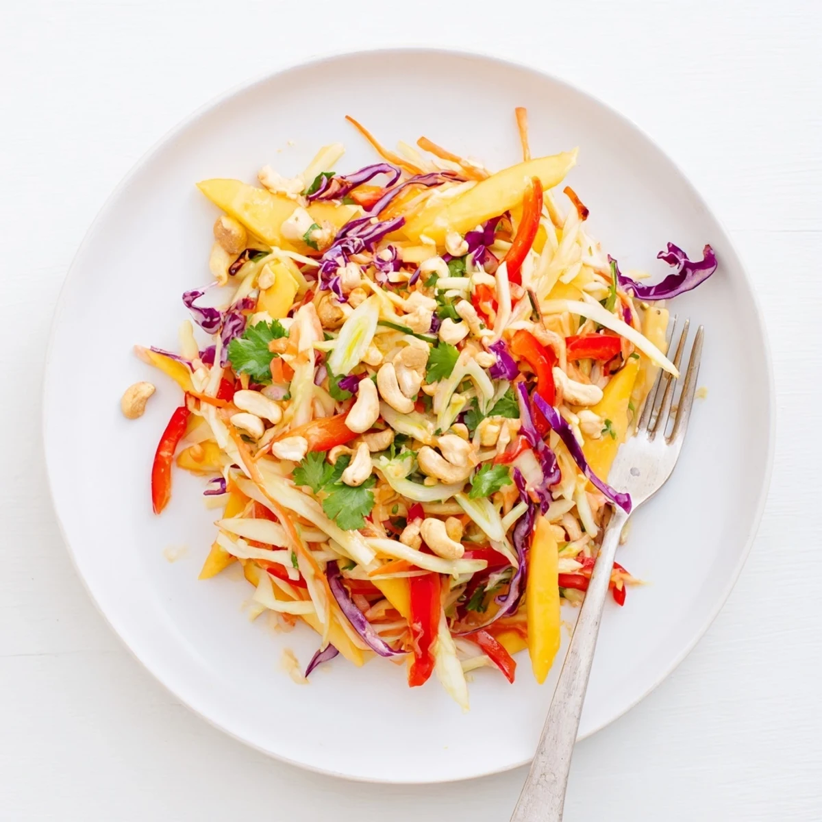 Colorful mango slaw bowl with crisp red cabbage, carrots, and lime drizzle on white background
