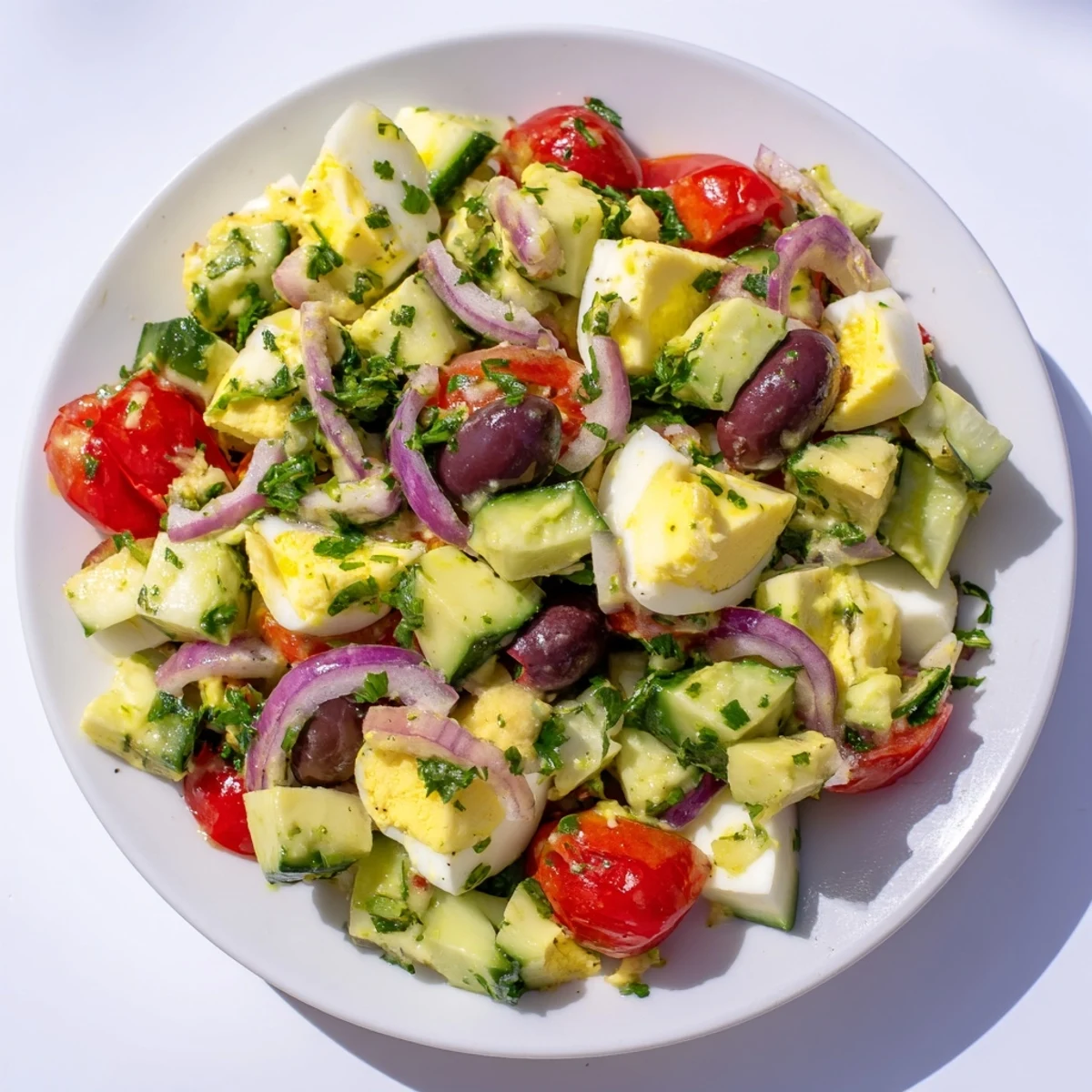 Simple zesty Mediterranean avocado egg salad served in a bowl with crisp red onion and cucumber pieces
