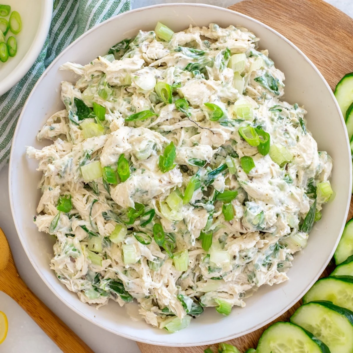 Creamy green goddess chicken salad dip topped with fresh herbs and sliced vegetables in a white serving bowl
