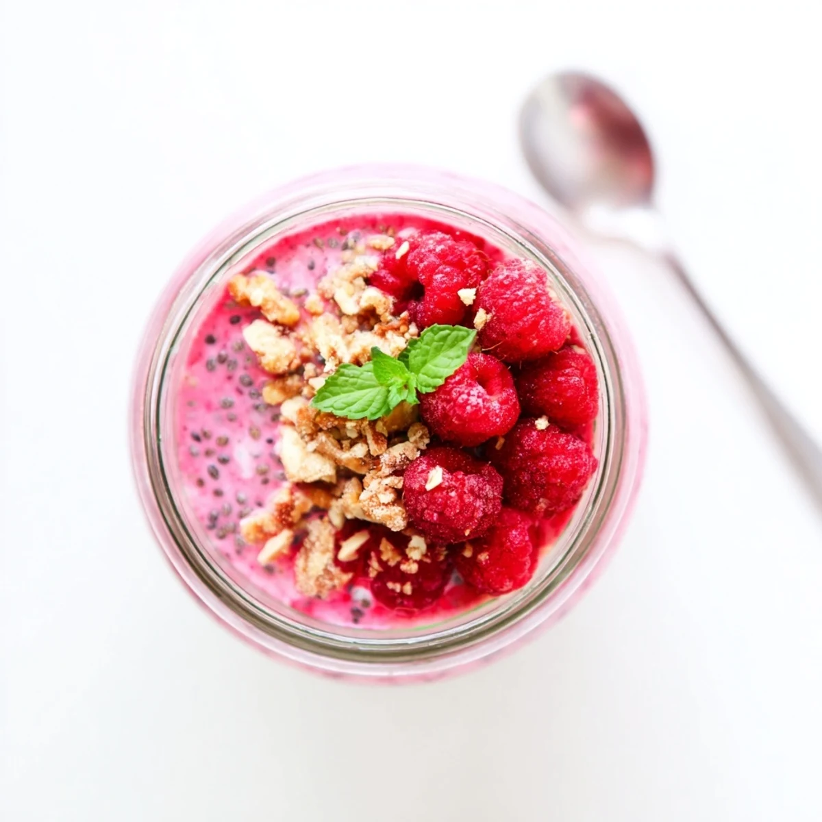 Creamy raspberry chia pudding topped with fresh berries and mint in glass jars