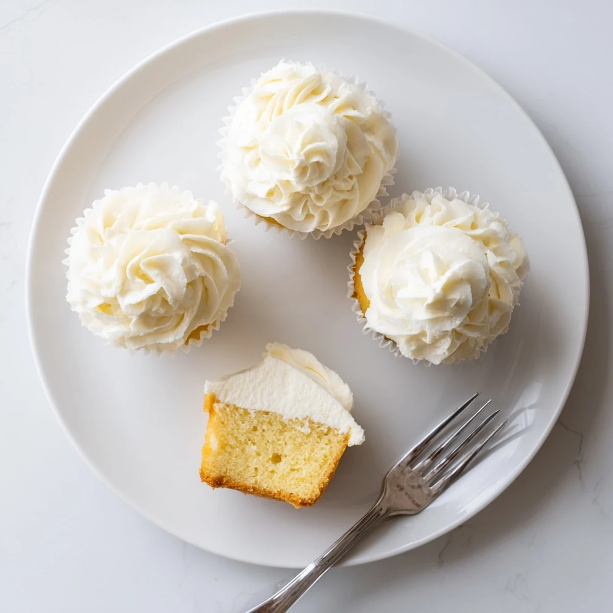 Light and fluffy vanilla cupcakes topped with swirls of creamy vanilla buttercream frosting on a white plate