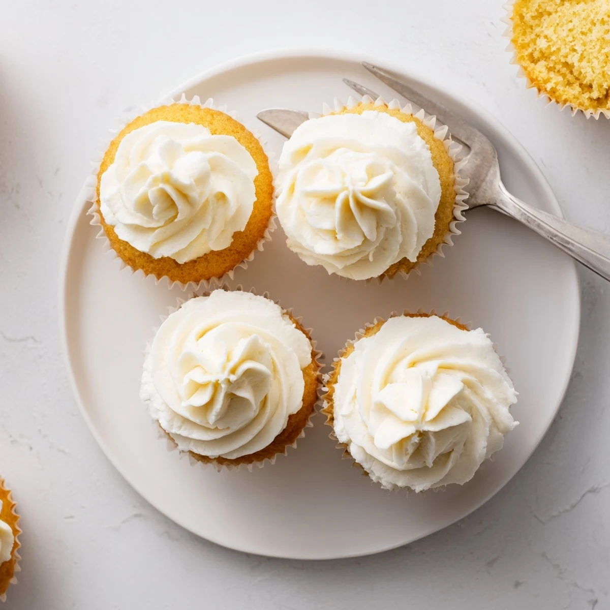 A batch of twelve freshly baked vanilla cupcakes with smooth white frosting piped in elegant swirls