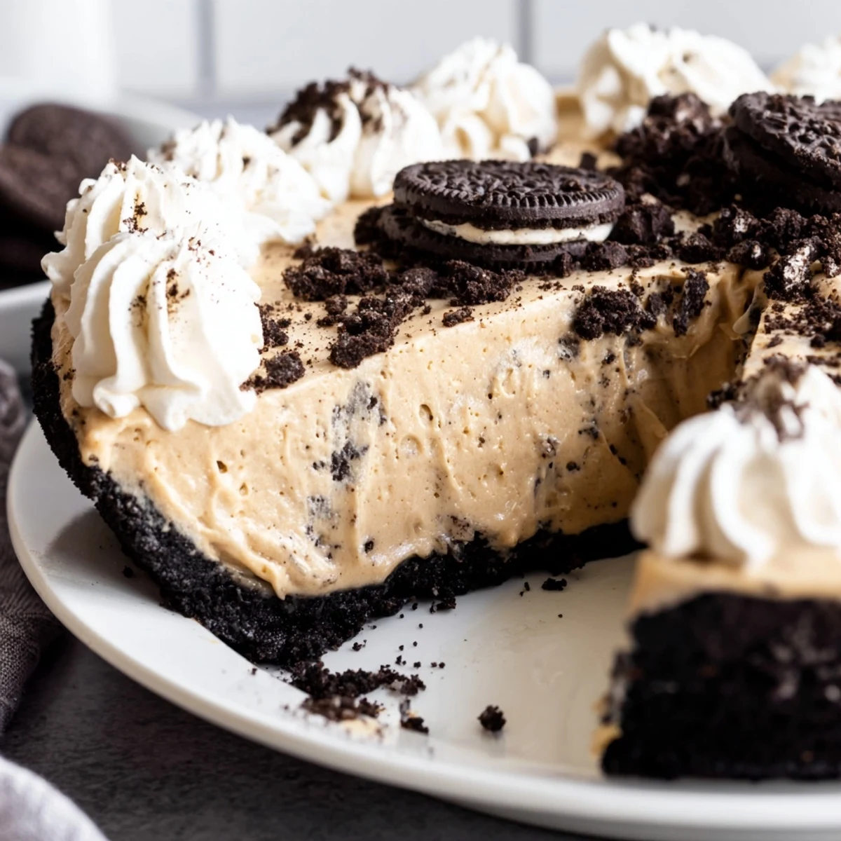Creamy peanut butter Oreo pie sliced and topped with fluffy whipped cream and cookie crumbles