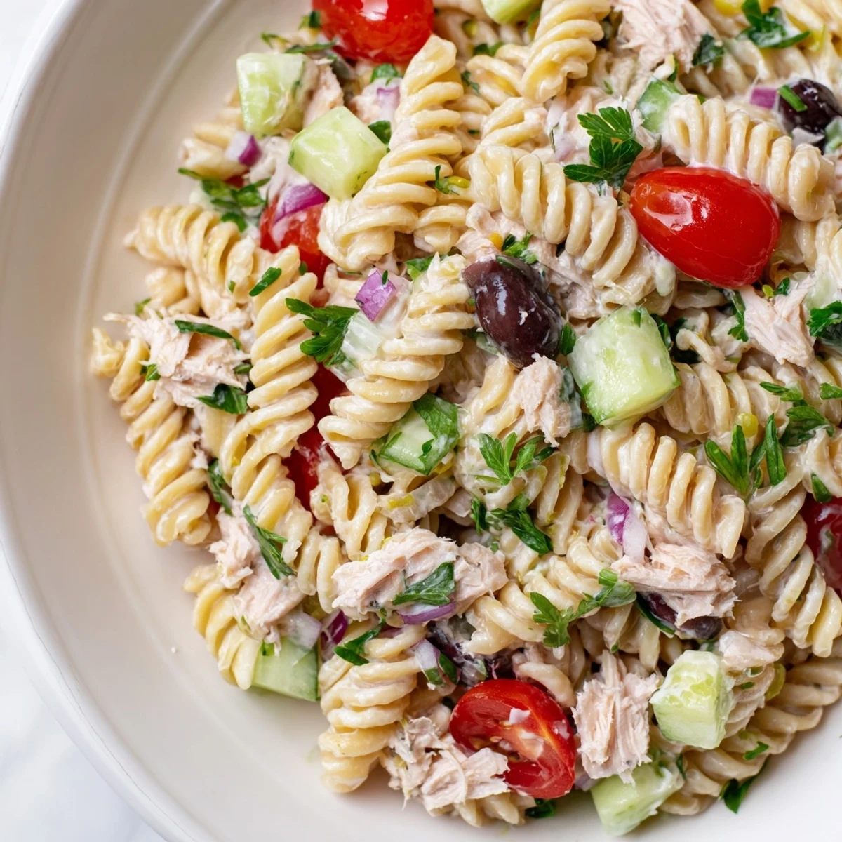 Creamy tuna pasta salad in a serving bowl with fresh vegetables and herbs