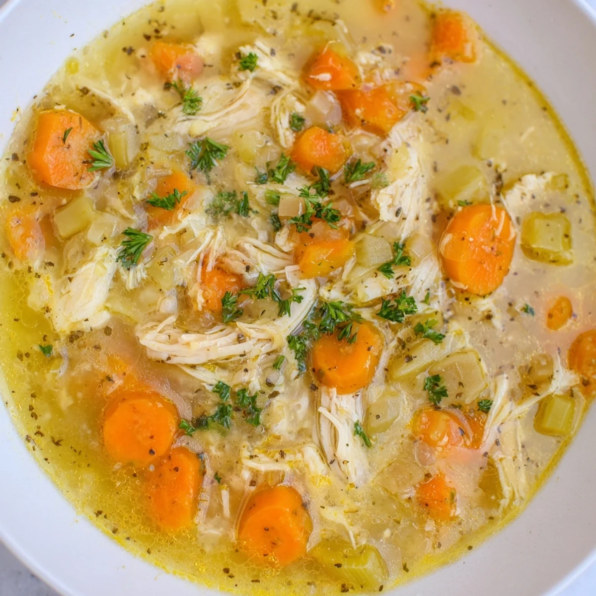 Golden chicken soup with tender vegetables and bright lemon slices steaming in a slow cooker