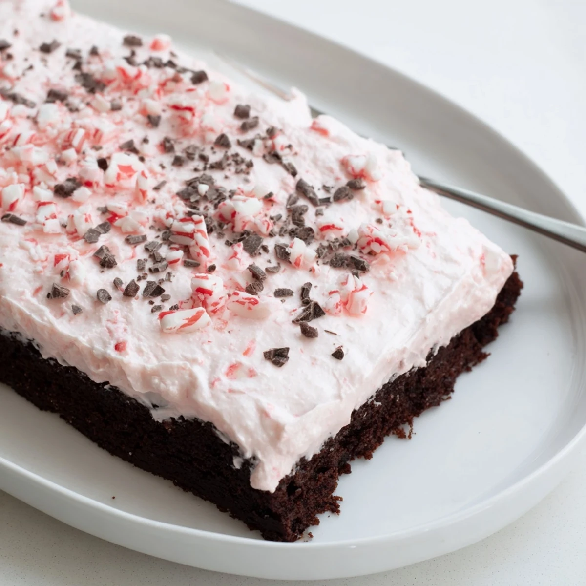 Slice of Peppermint Poke Cake with fluffy whipped topping and peppermint crunch
