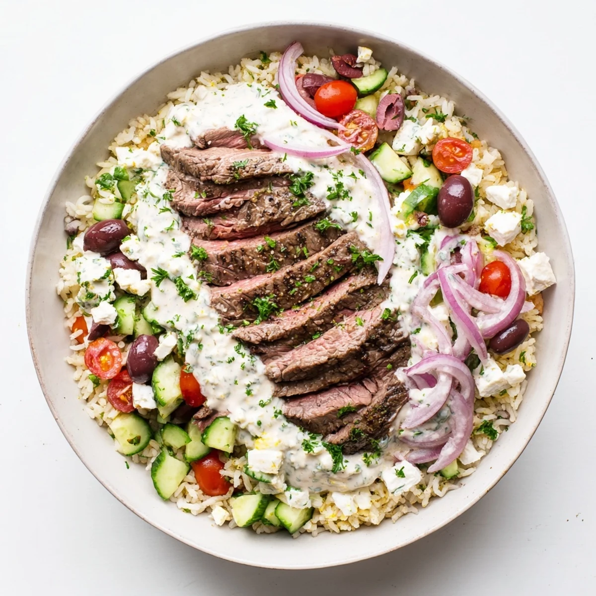 Sliced steak bowl featuring cherry tomatoes cucumber olives and creamy yogurt sauce drizzle
