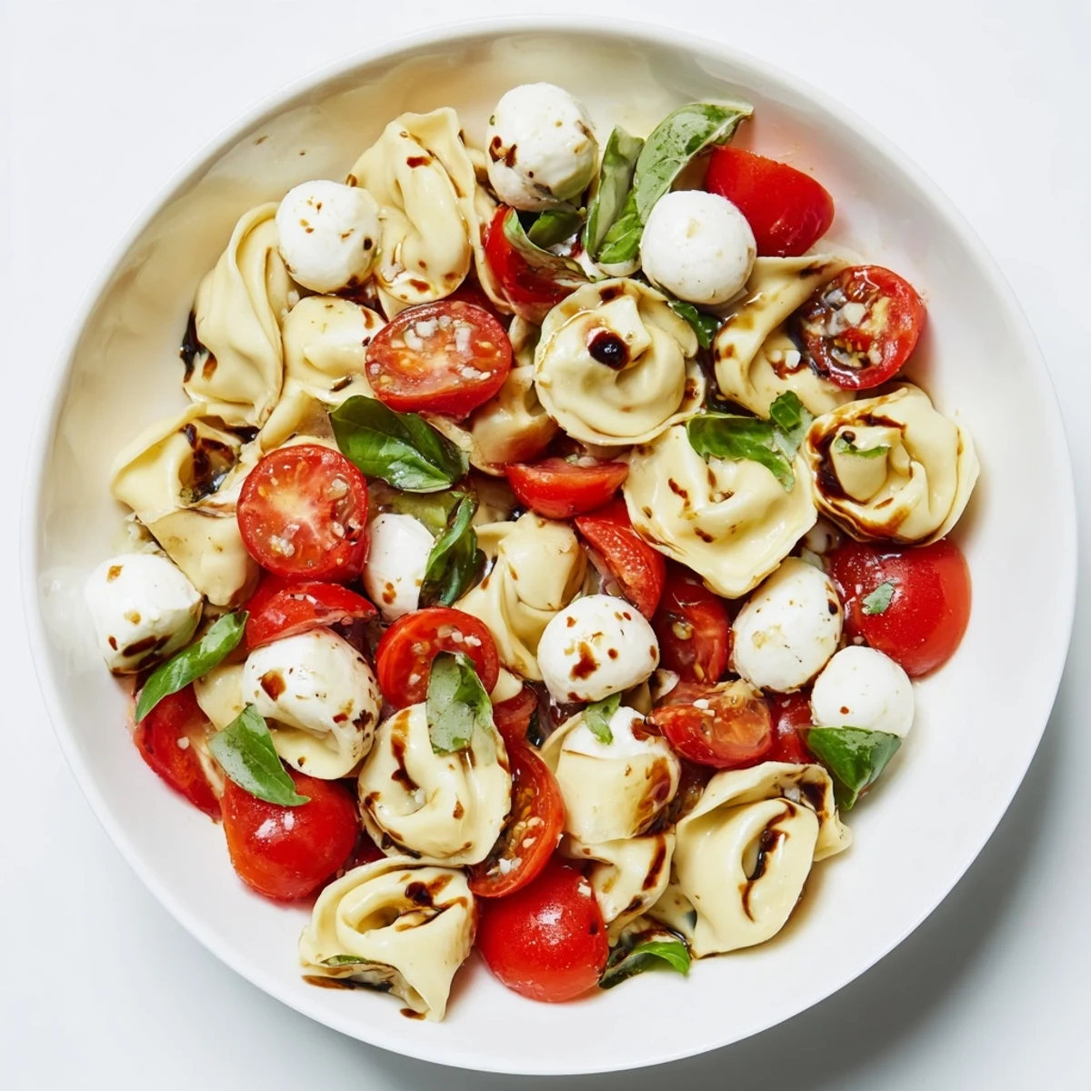 Colorful bowl of cheese tortellini salad tossed with juicy tomatoes and fresh basil for summer meals