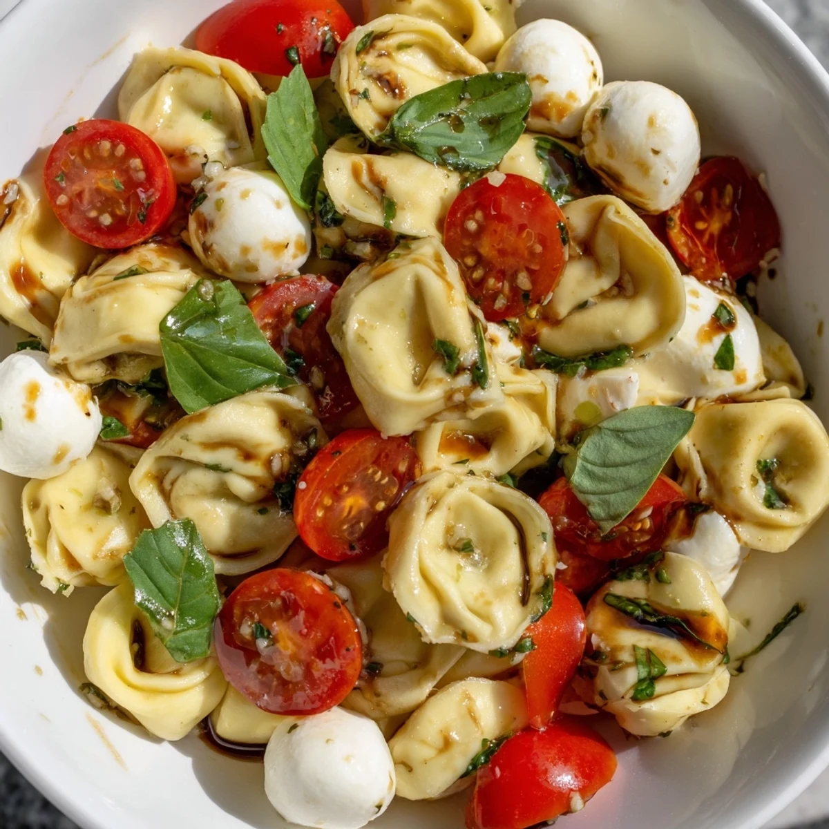 Fresh tortellini Caprese salad with cherry tomatoes, mozzarella balls, and basil leaves drizzled with balsamic glaze